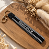 Equestrian Jewelry sleutelhanger Coach en or in stevig lint met geborduurde tekst en goudkleurige ringen