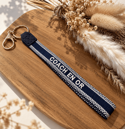Equestrian Jewelry sleutelhanger Coach en or in stevig lint met geborduurde tekst en goudkleurige ringen