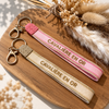 Equestrian Jewelry sleutelhanger Cavalière en or in stof met geborduurde tekst en goudkleurige ringen