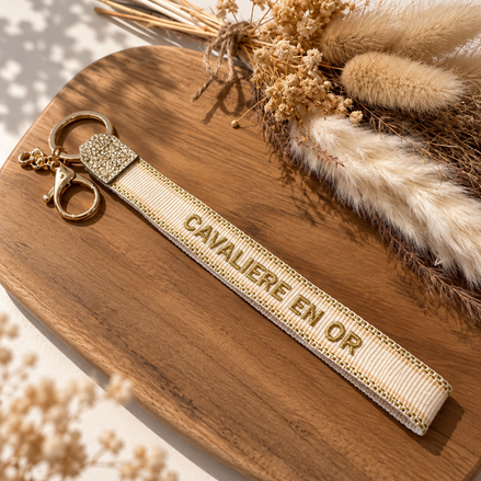 Equestrian Jewelry sleutelhanger Cavalière en or in stof met geborduurde tekst en goudkleurige ringen