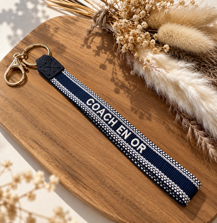 Equestrian Jewelry sleutelhanger Coach en or in stevig lint met geborduurde tekst en goudkleurige ringen
