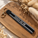 Equestrian Jewelry sleutelhanger Coach en or in stevig lint met geborduurde tekst en goudkleurige ringen